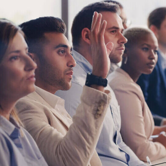 Audience, conference and question of a business man with hand up at a seminar, workshop or training. Diversity men and women crowd at a presentation for learning, knowledge and faq discussion.